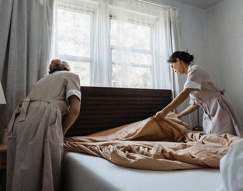 Domestic Helpers Neatly Tidying Up a Bed Near a Window
